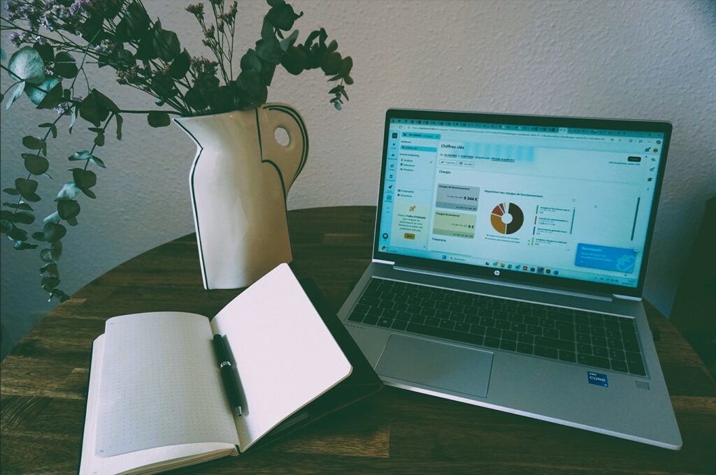 Un ordinateur avec des KPI affichés et un carnet ouvert posé sur une table