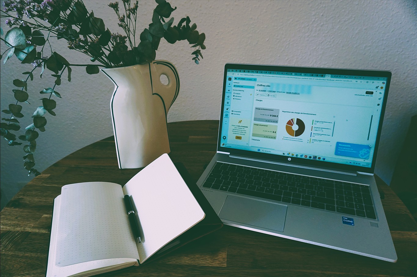 Un ordinateur avec des KPI affichés et un carnet ouvert posé sur une table