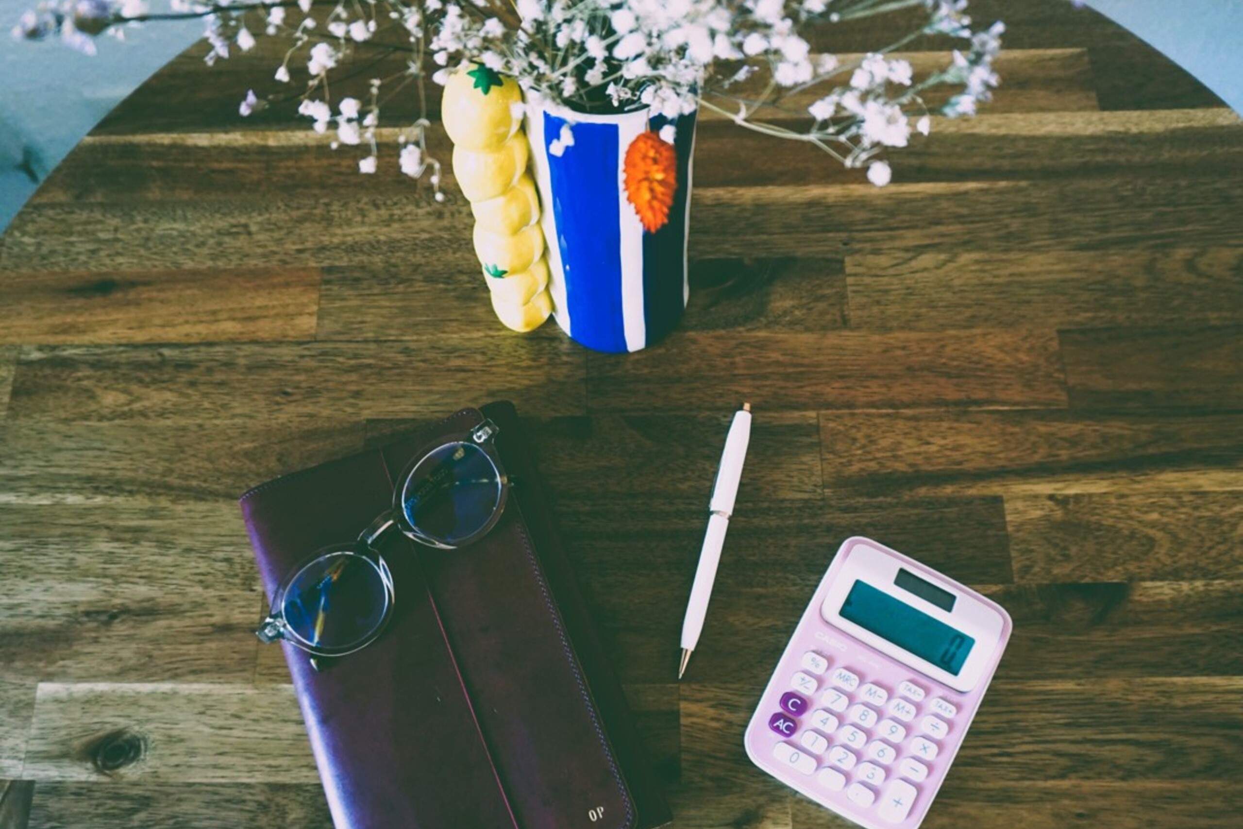 Image vue d'en haut d'une table joliment décorée avec un carnet, stylo, lunettes, calculette et pot de fleurs